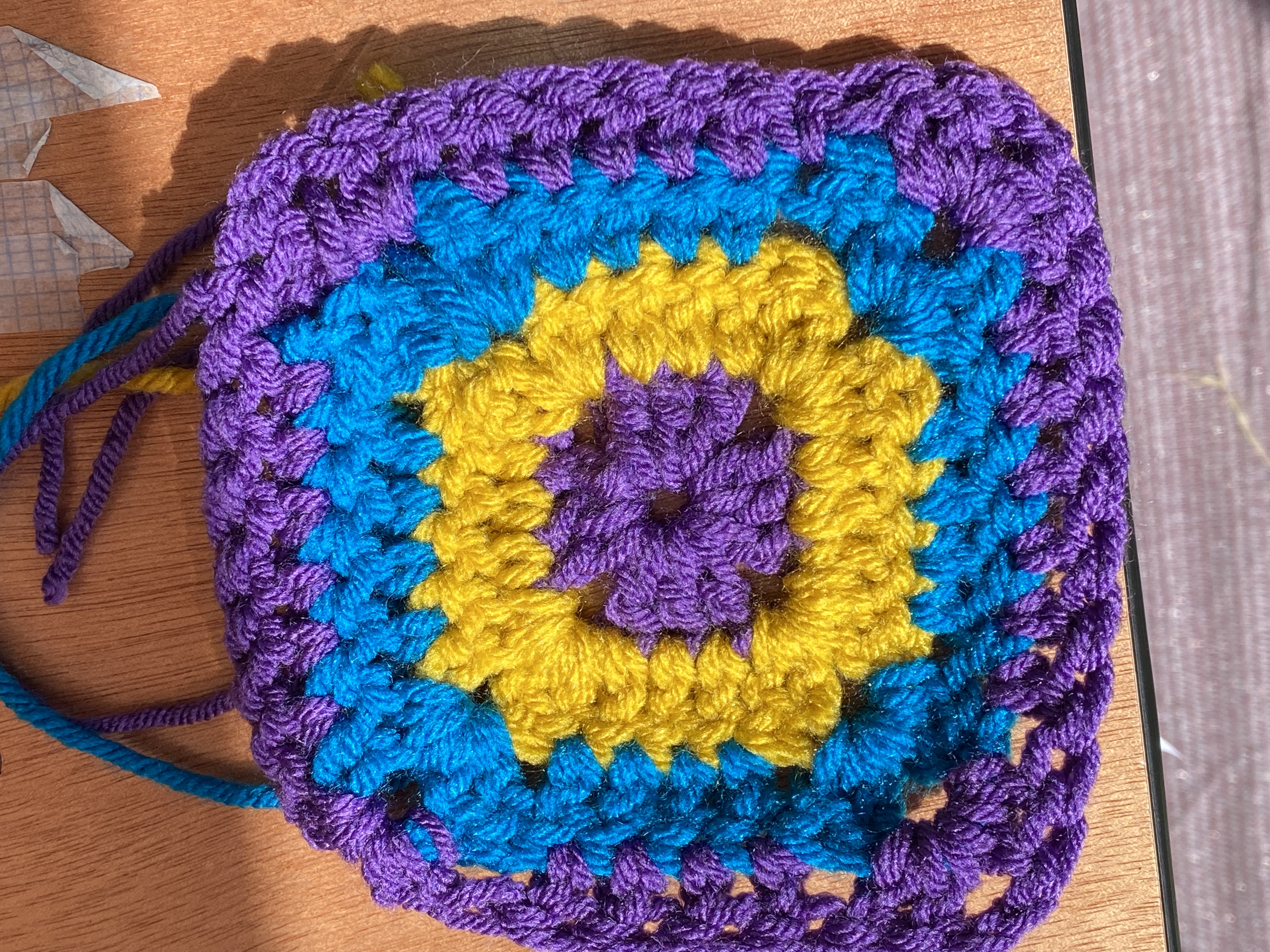 Granny square with a purple centre, yellow surround, turquoise third row and purple outer row